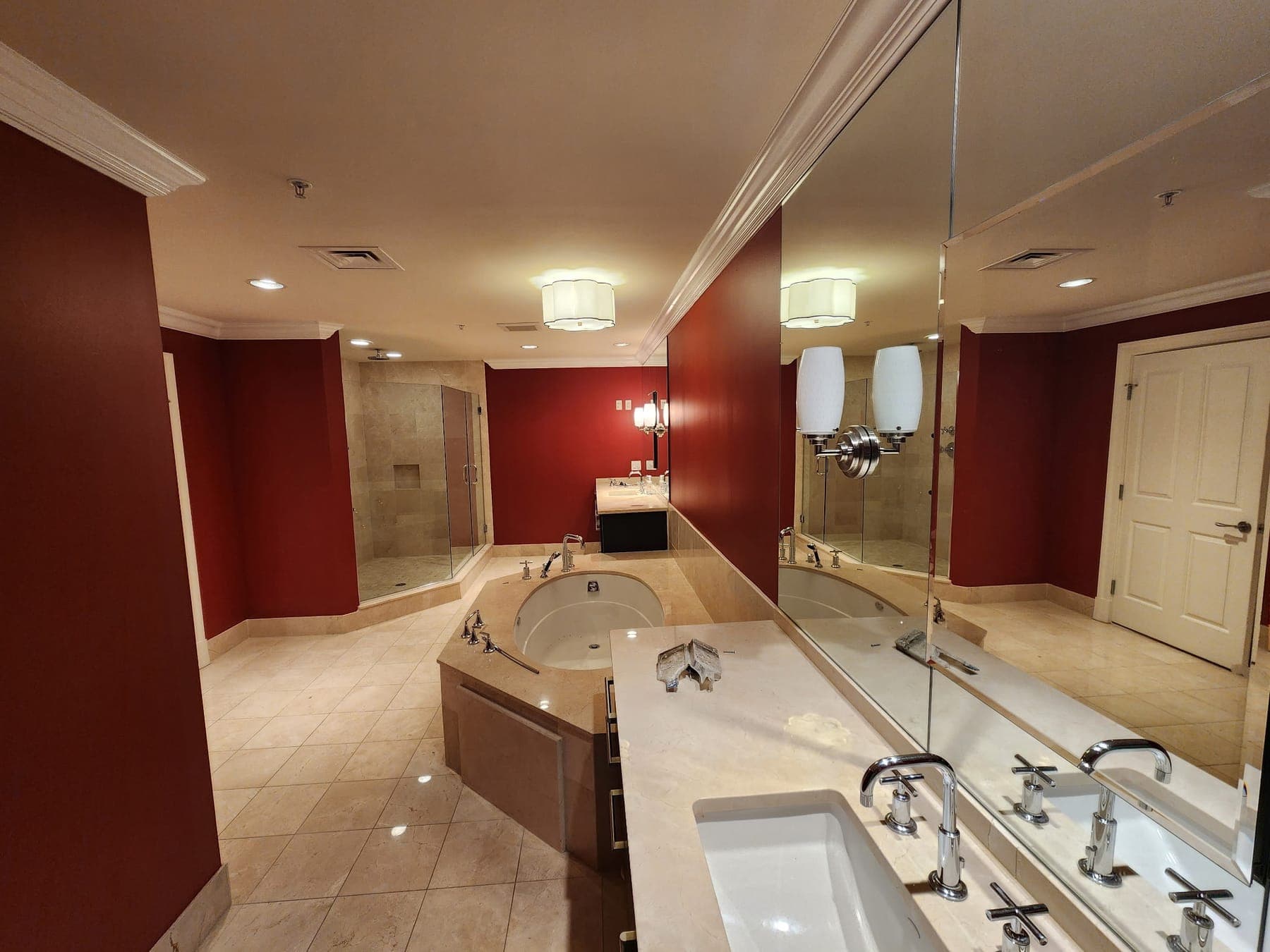 Primary bathroom with deep red walls, marble tub deck and glass shower by Elite Finishes